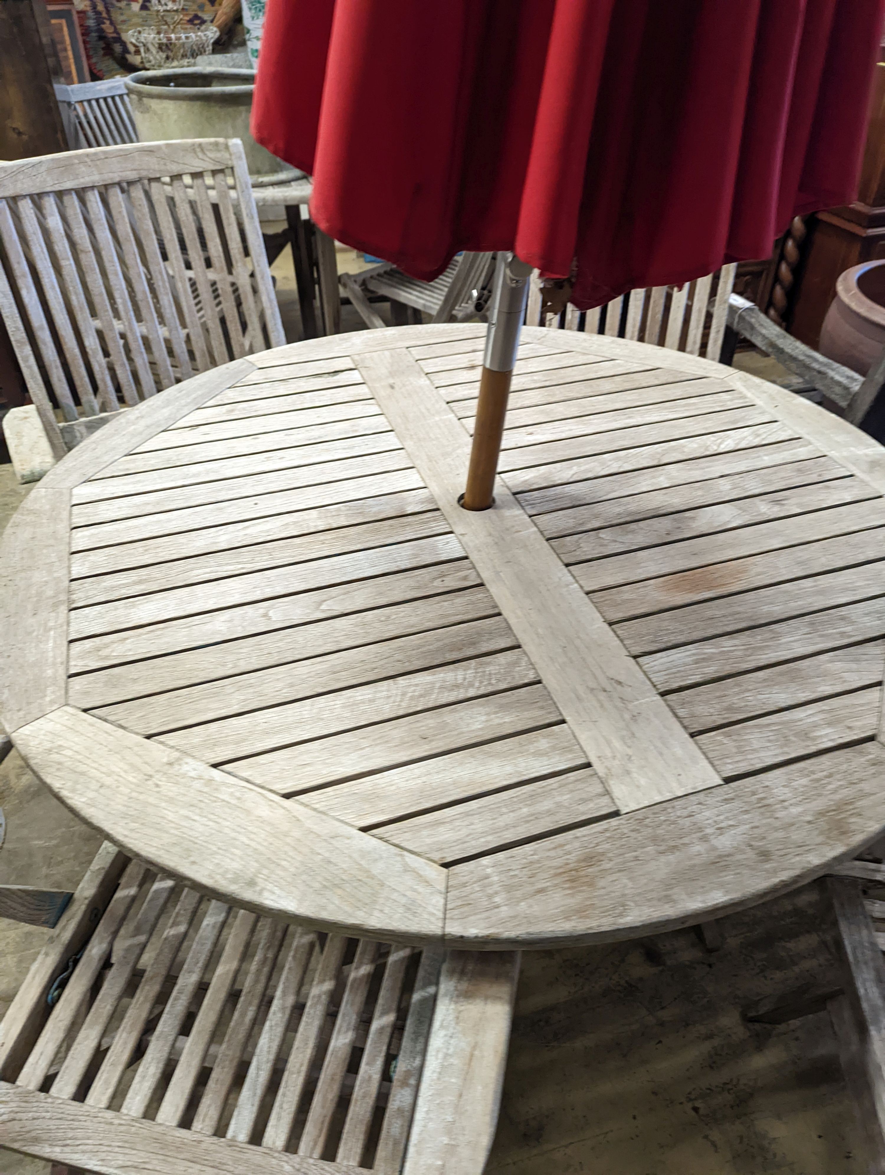 A circular weathered teak folding garden table, diameter 120cm, height 74cm, four folding elbow chairs and a parasol